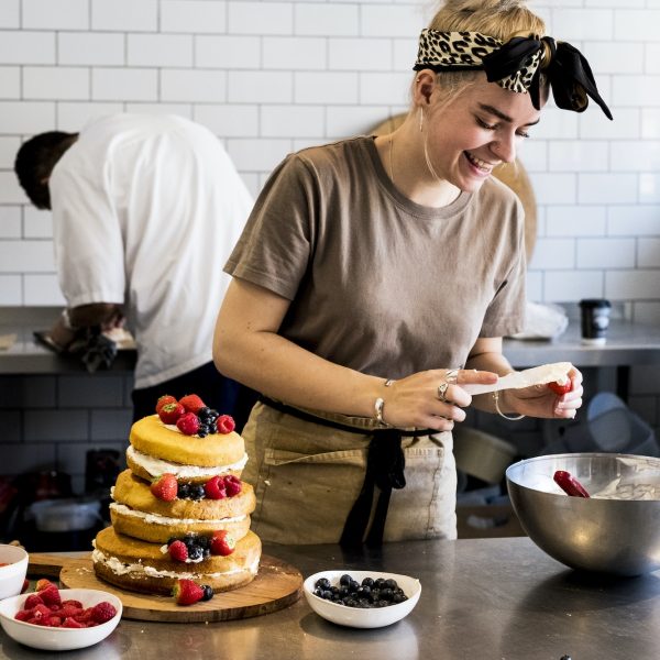 a-cook-working-in-a-commercial-kitchen-assembling-a-layered-sponge-cake-with-fresh-fruit-.jpg